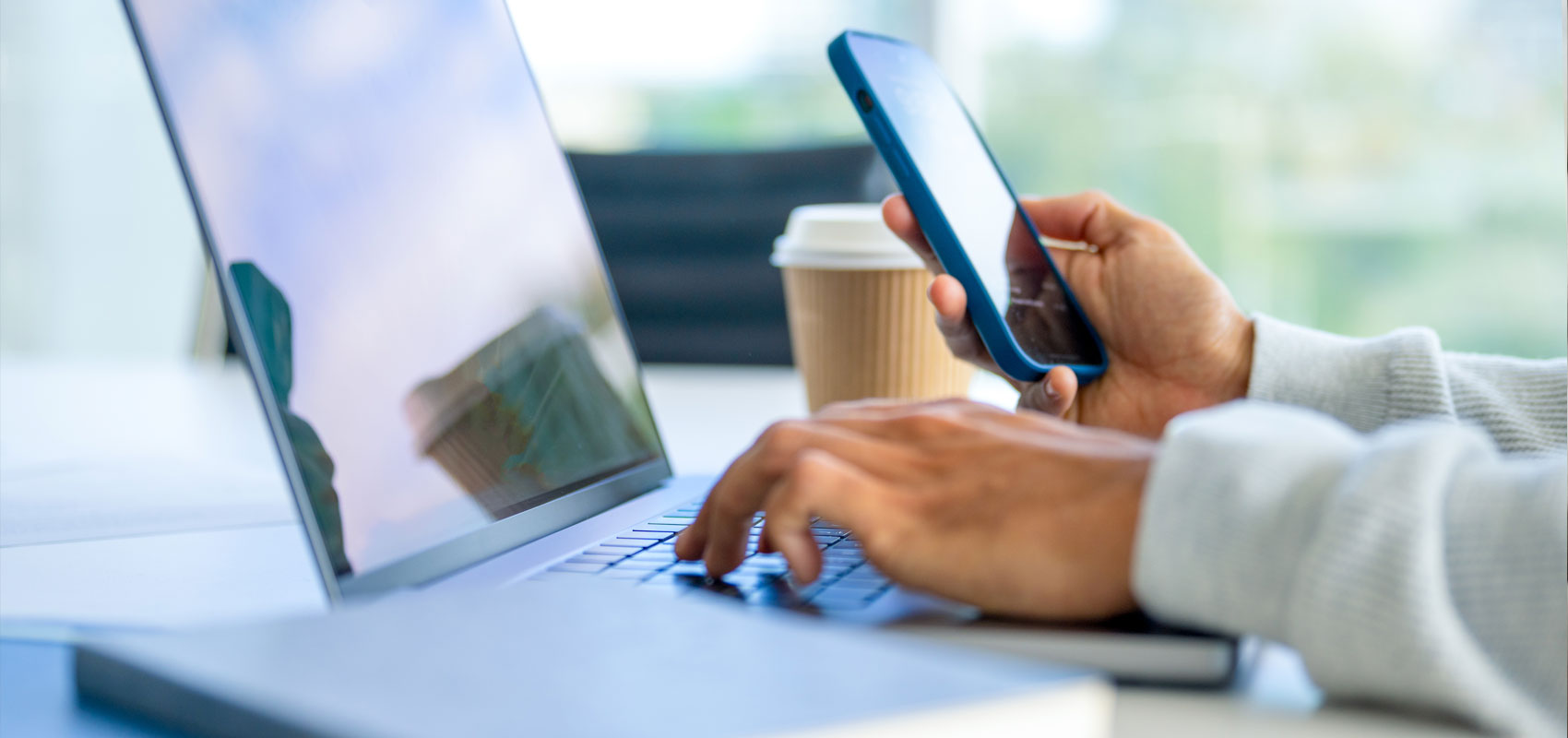 Person at a desk using a laptop and phone at the same time