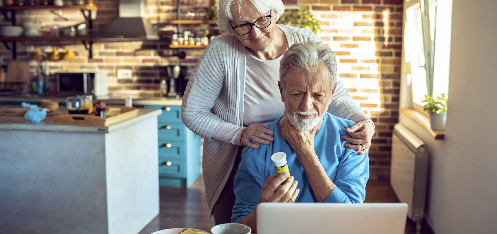 Senior couple with husband holding a prescription bottle looking at laptop