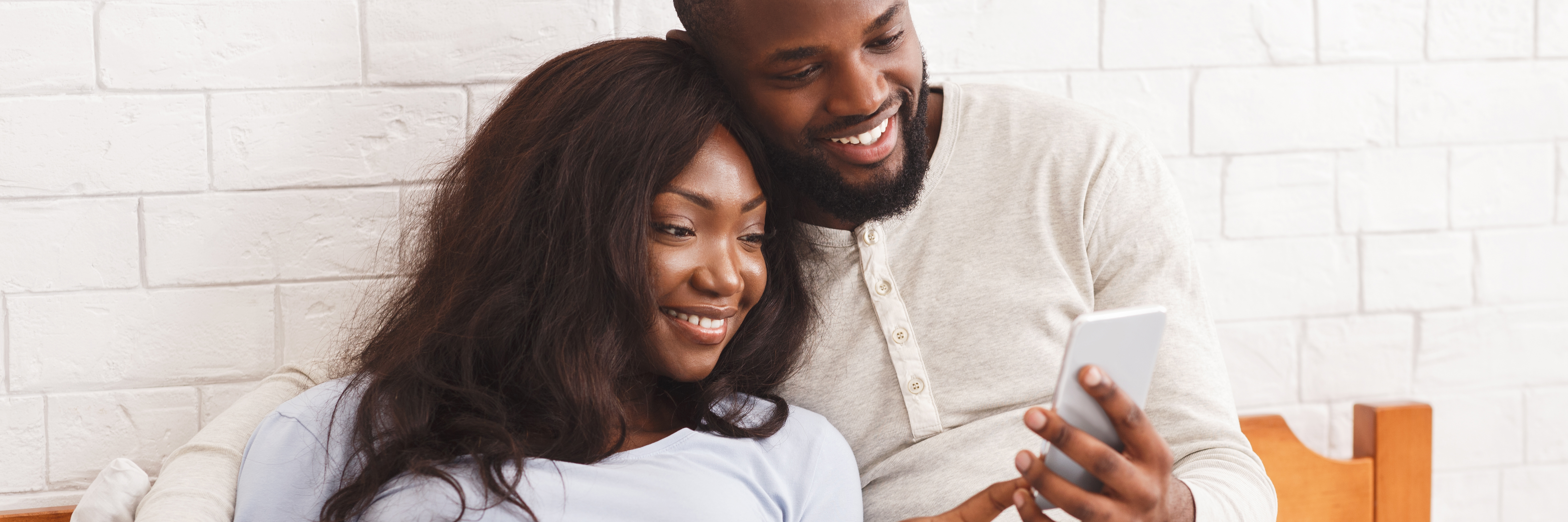 Two adults smile while looking at a mobile device.