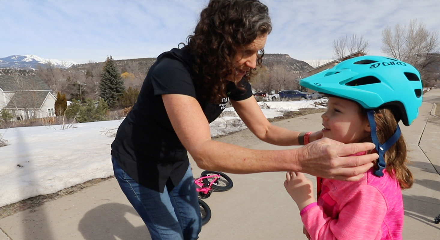 A woman helps a school-age girl secure her bicycle helmet