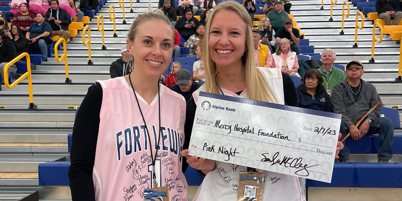 Two female athletes pose with a donation made out to Mercy Health Foundation