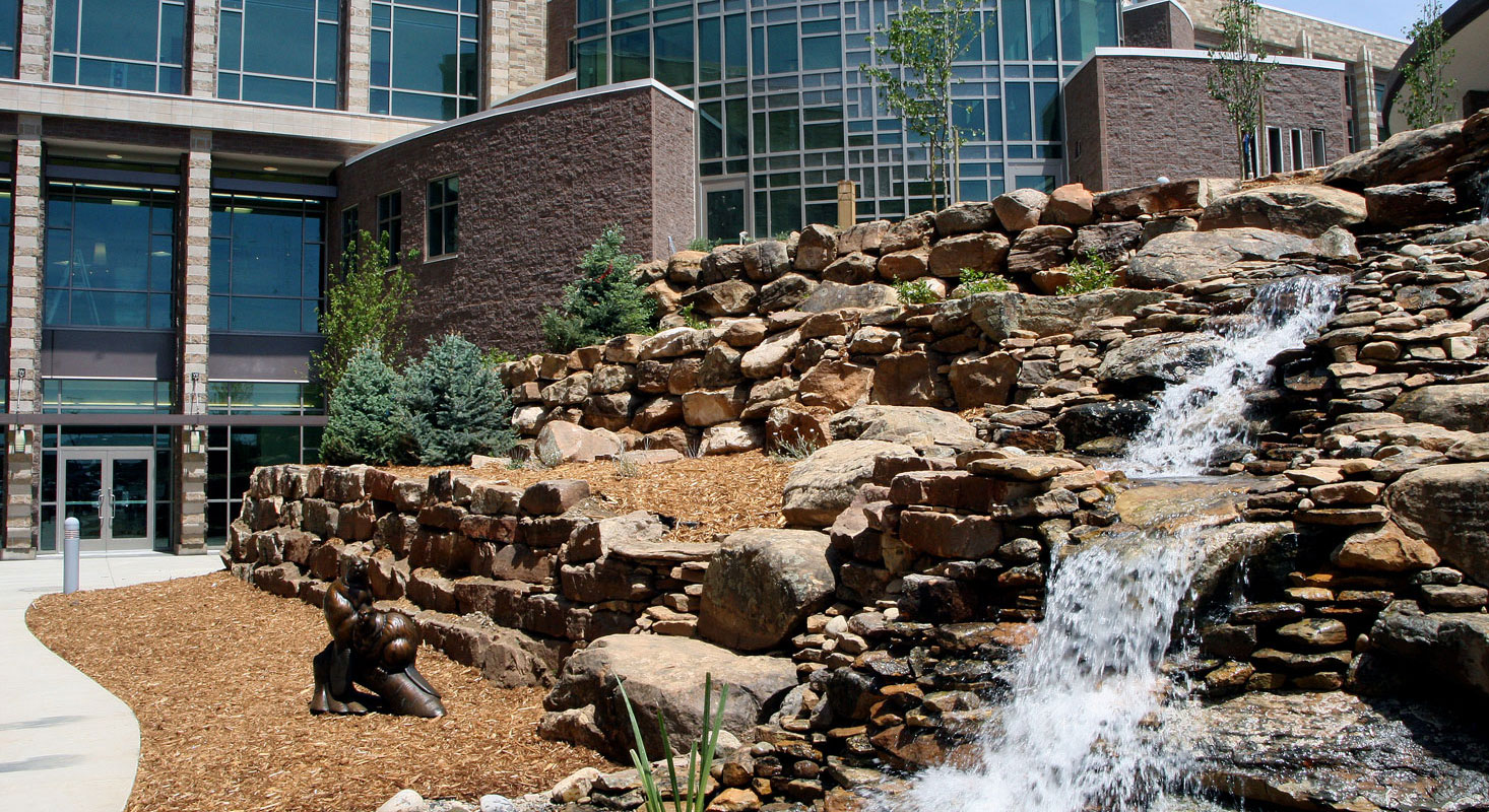 A rushing waterfall cascades down red rocks in front of the hospital building