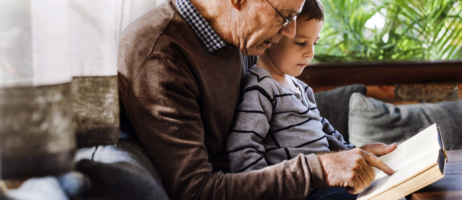 An elderly man and his grandson read in a home setting