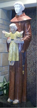 A statue of St Francis in a brown habit, holding the infant Jesus in front of him