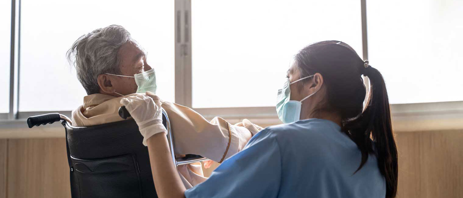 A nurse bends to comfort a patient in a wheelchair